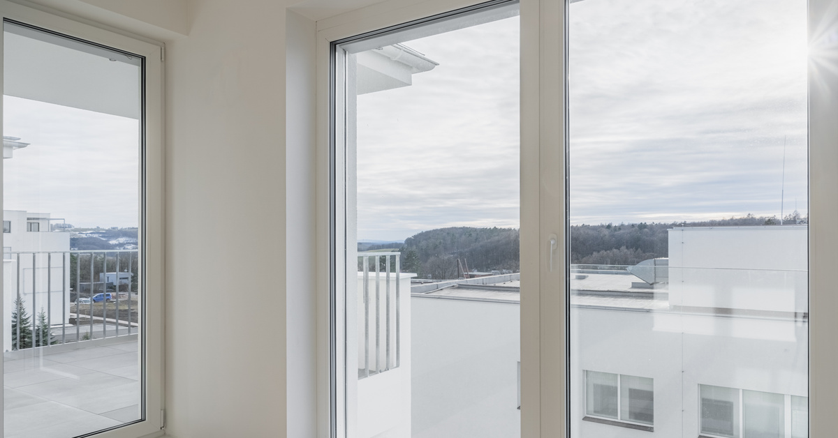 A white room in an apartment or condo with large windows nearly spanning floor to ceiling, looking out over the landscape.