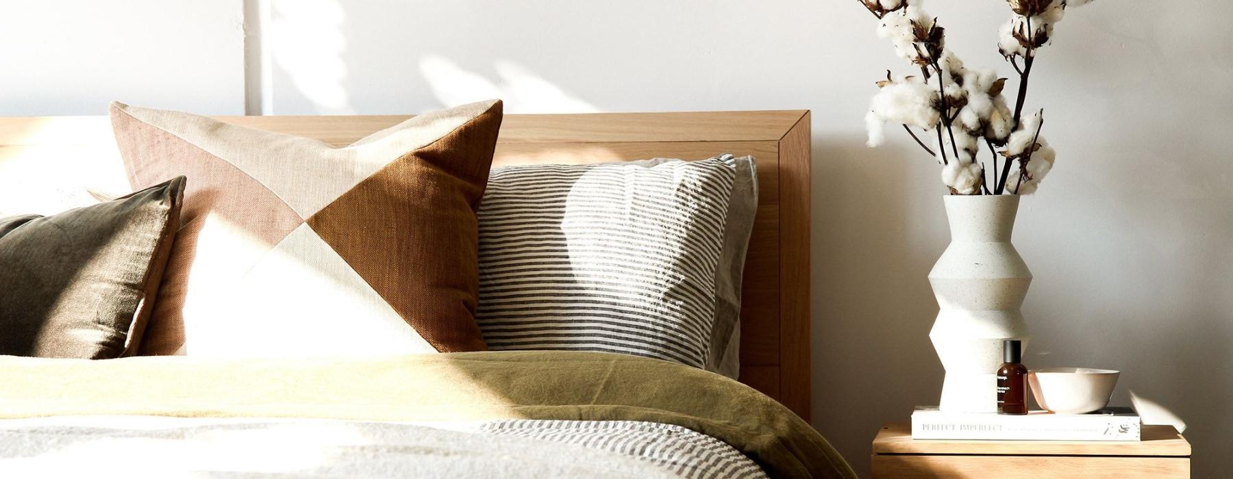 swath of sunlight shines across a well made bed and bedside table with a vase of cotton plants