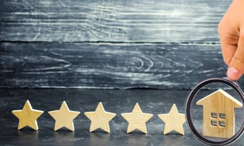 digtigardqozbllc-391034-wood-cutout-stars-thumbnail A hand holds a magnifying glass up to a wooden cutout of a house. Five wooden star cutouts line up next to it.
