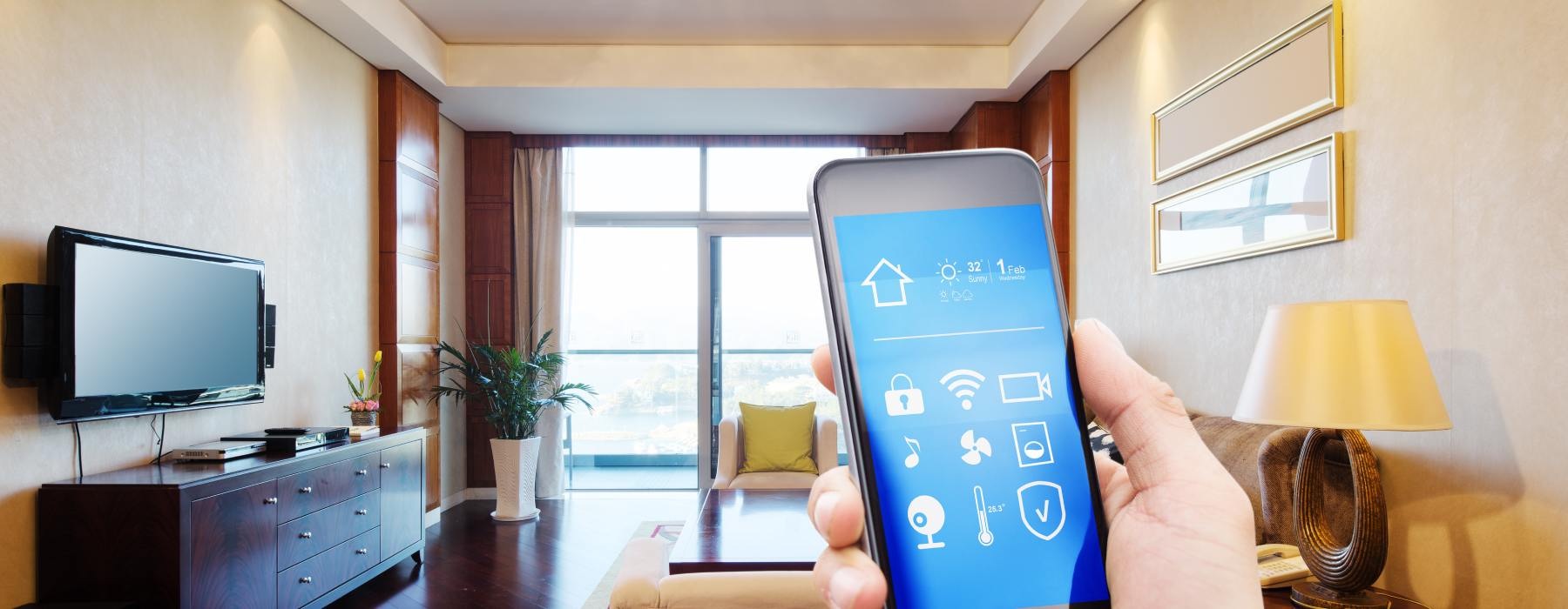 A wide shot of an apartment room with a close-up of a person's hand holding a smartphone in the foreground.