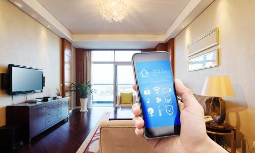 A wide shot of an apartment room with a close-up of a person's hand holding a smartphone in the foreground.