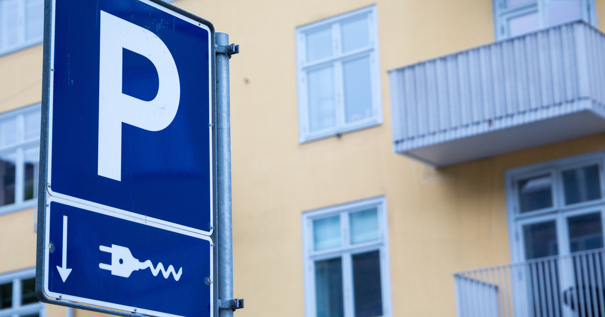 digtigardqozbllc-299695872-blue-parking-sign-image-b1 A blue parking sign with an electrical charging symbol beneath it outside a group of apartment windows.