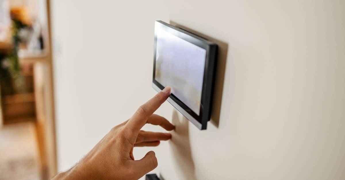 digtigardqozbllc-391034-hand-touchscreen-wall-image-b1 A close-up of a hand reaching a finger out to touch a touchscreen mounted to a beige-colored wall.